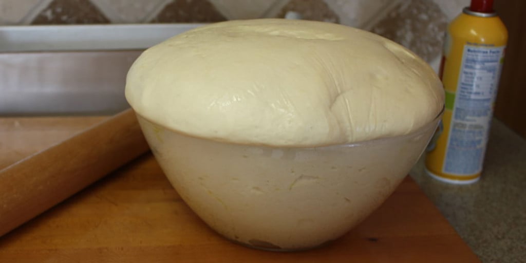 Bread dough risen over the sides of glass bowl.