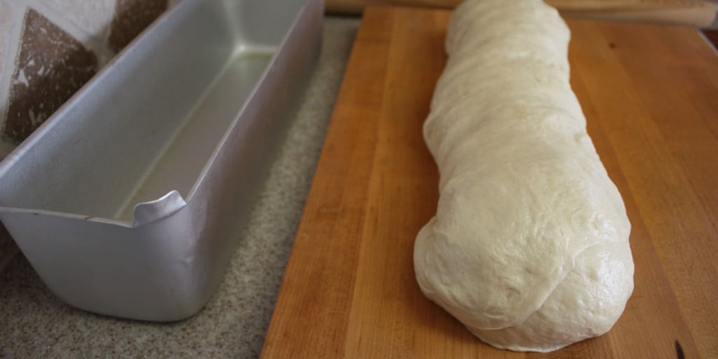 Bread dough shaped into a loaf on a wooden board.