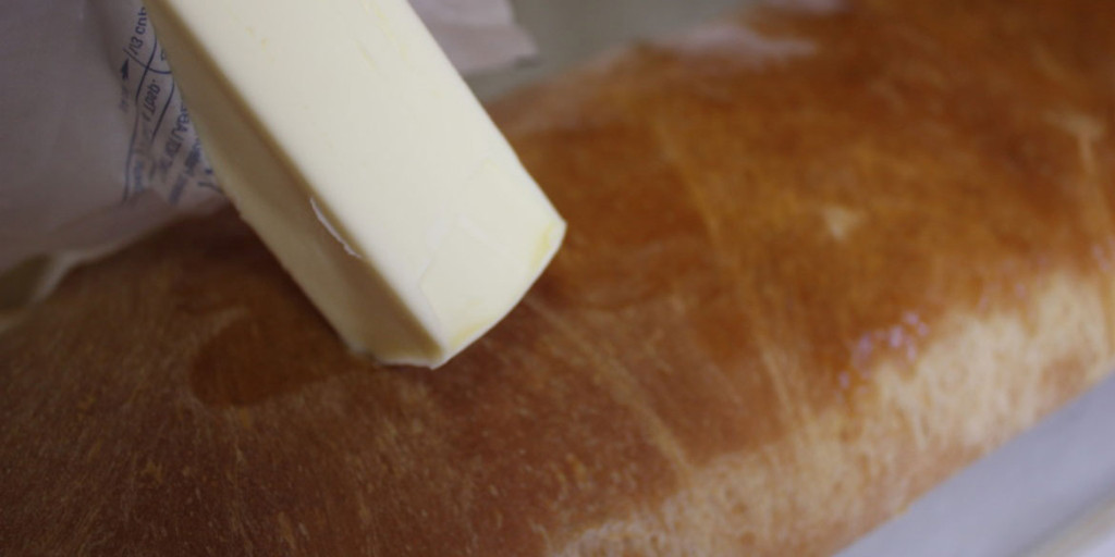 Butter being rubbed on the top crust of the sandwich bread.