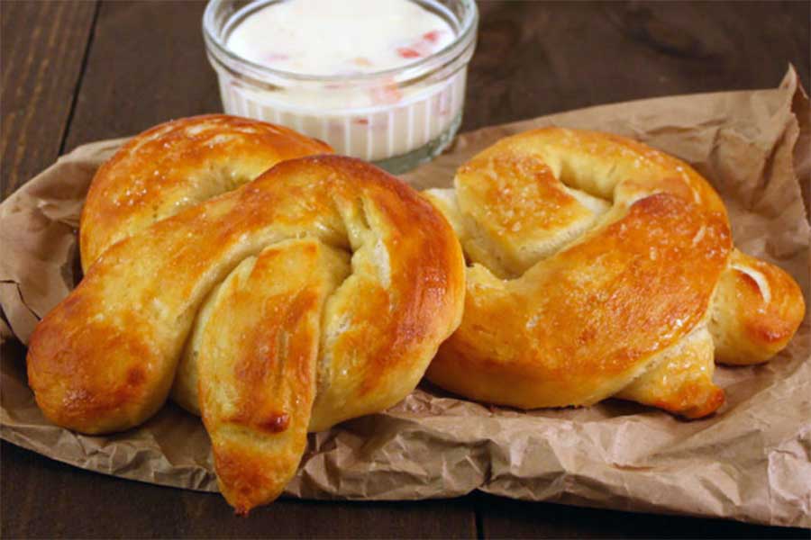 Soft Pretzels on brown paper with cheese dip in background.