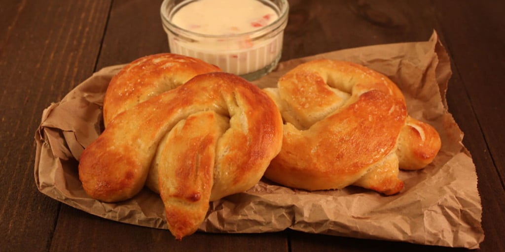Soft pretzels on brown paper with a ramekin of cheese dip.