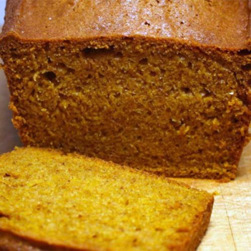 Pumpkin bread with a slice cut on a cutting board.