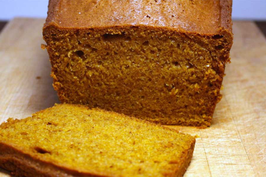 Pumpkin bread with a slice cut on a cutting board.