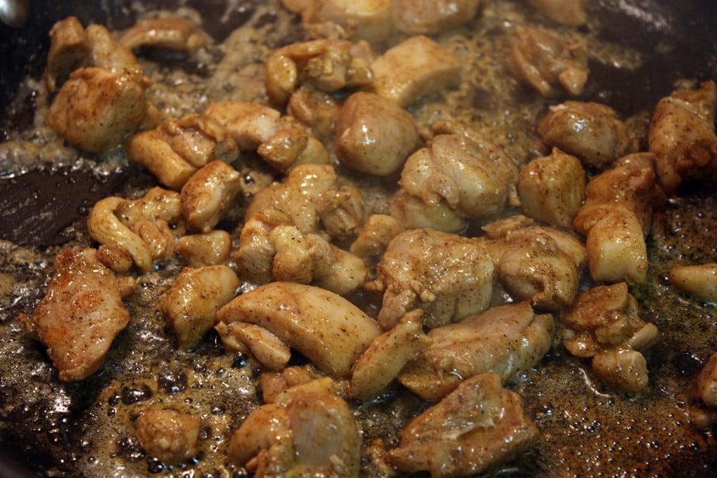 Seasoned chicken pieces cooking in a skillet.