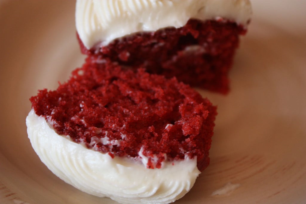 Red velvet cupcake cut in half on a cream colored plate.