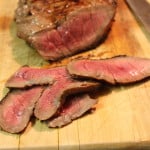 Sliced medium-rare London Broil on a wooden cutting board.