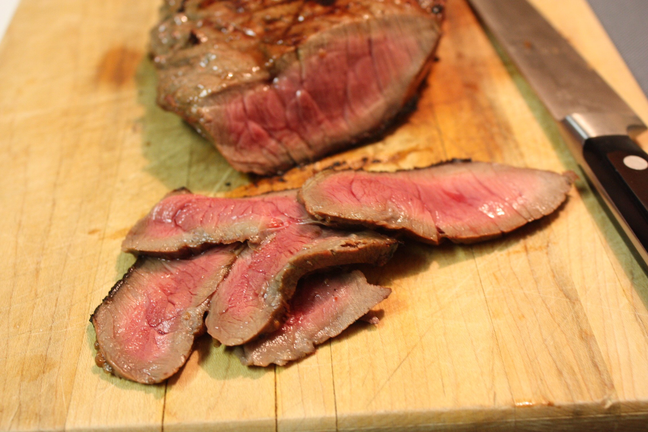 Sliced medium-rare London Broil on a wooden cutting board.