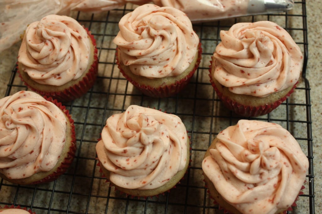 Fresh strawberry cupcakes topped with fresh strawberry buttercream icing on a wire rack.