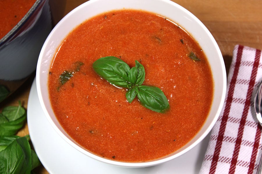 Creamy tomato basil soup with a basil garnish in a white bowl.