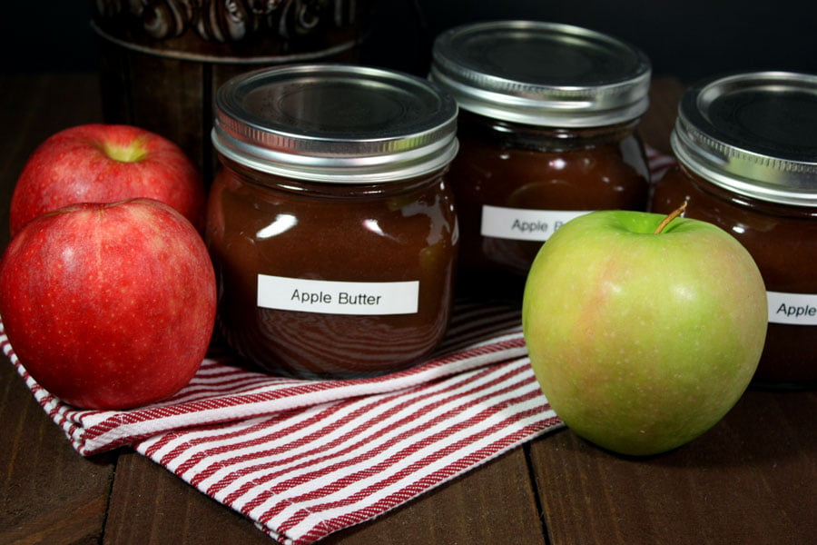 Slow cooker apple butter in mason jars surrounded by apples.