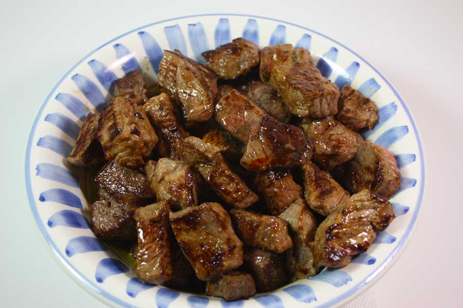 Browned cubed meat in a white bowl.