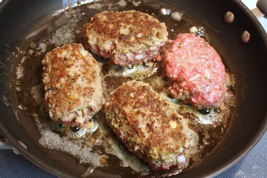Meat patties cooking in a skillet.