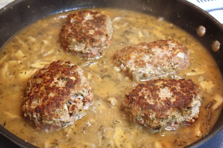 Meat patties in the skillet with the gravy ingredients.