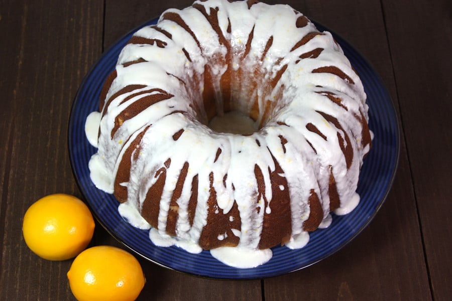 Meyer Lemon Bundt Cake on a cake dish with Meyer lemons on the side.