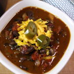 Vegetarian chili, garnished with cheese and jalapenos, in a white bowl.