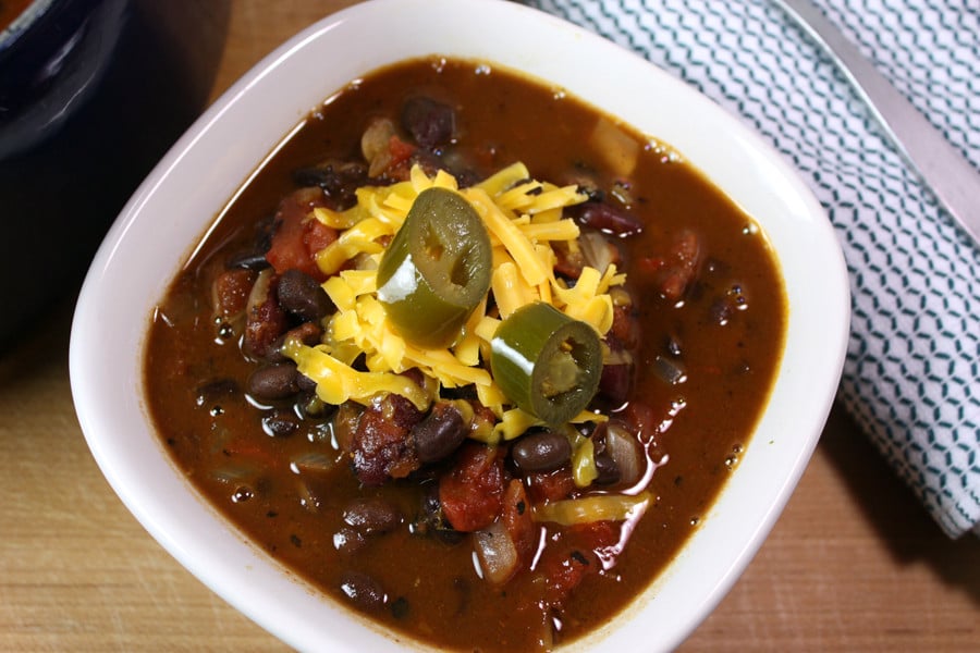 Vegetarian chili, garnished with cheese and jalapenos, in a white bowl.