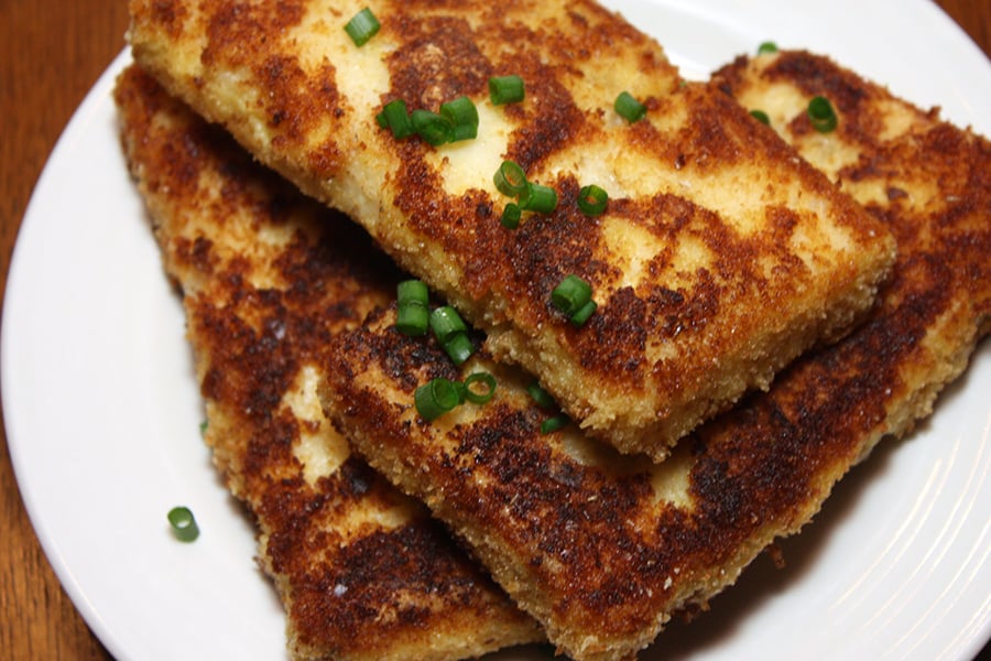 Fried Grit Cakes on a white plate garnished with green onion.