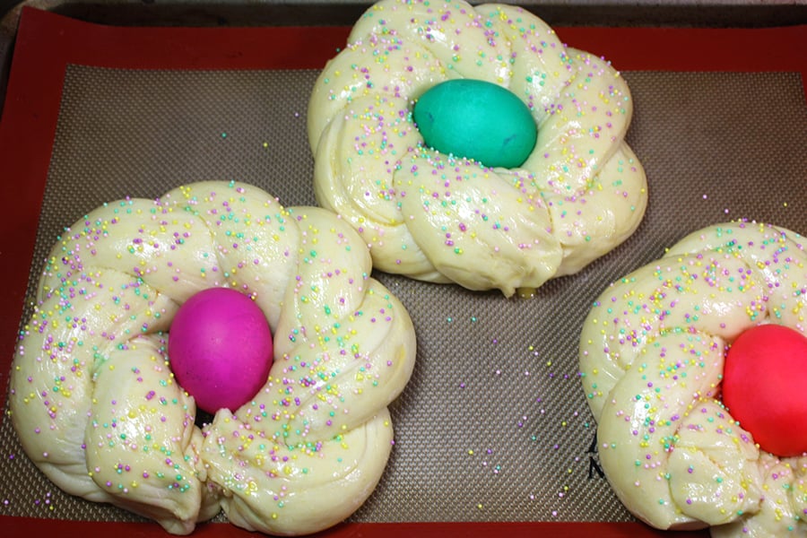 Risen, shaped dough with dyed eggs in the middle on a baking sheet.