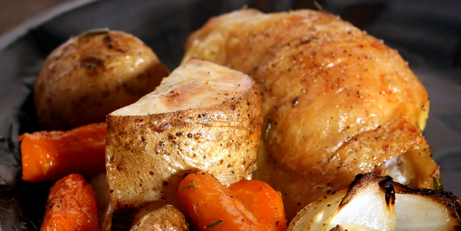 Roasted chicken thigh, potatoes, and carrots on a black plate.
