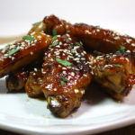 Honey Sriracha Wings on a white plate and a sesame garnish.