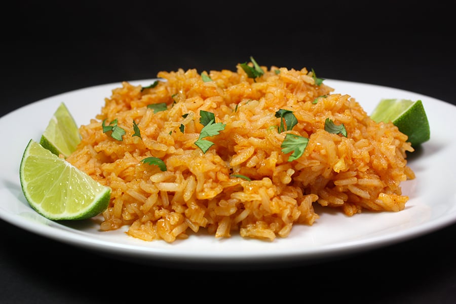 Restaurant style Mexican rice on a white plate with lime wedges as a garnish.