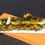 Turmeric chicken skewers on a white serving plate.