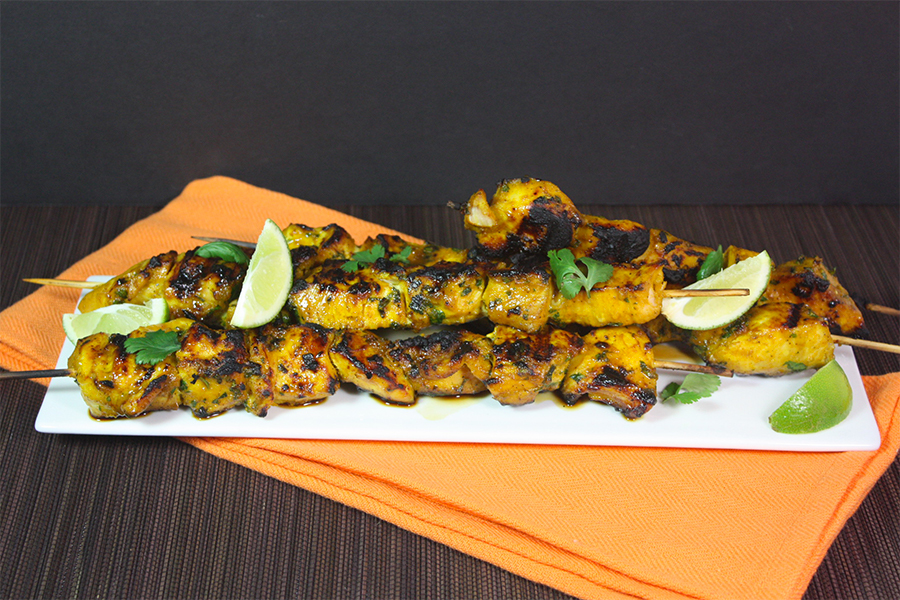 Turmeric chicken skewers on a white serving plate.