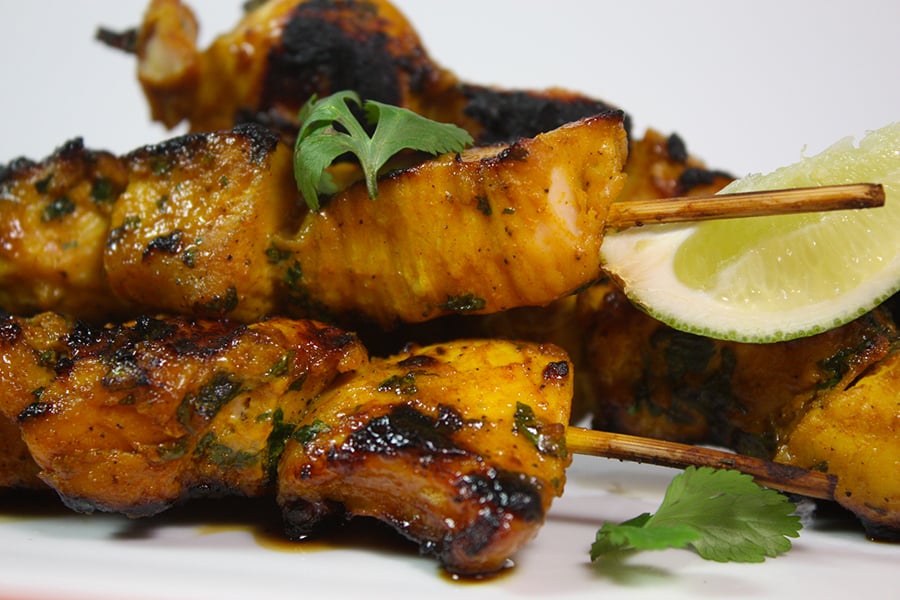 Turmeric Chicken Kabobs on a white platter garnished with parsley and lime wedges