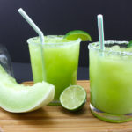 Honeydew margaritas in a short glass with a bottle of patron in the background.