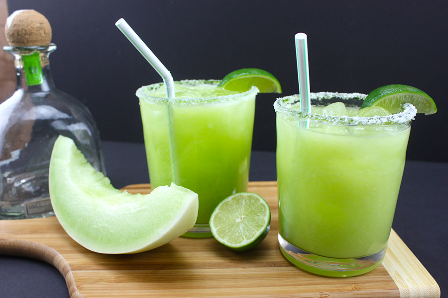 Honeydew margaritas in a short glass with a bottle of patron in the background.