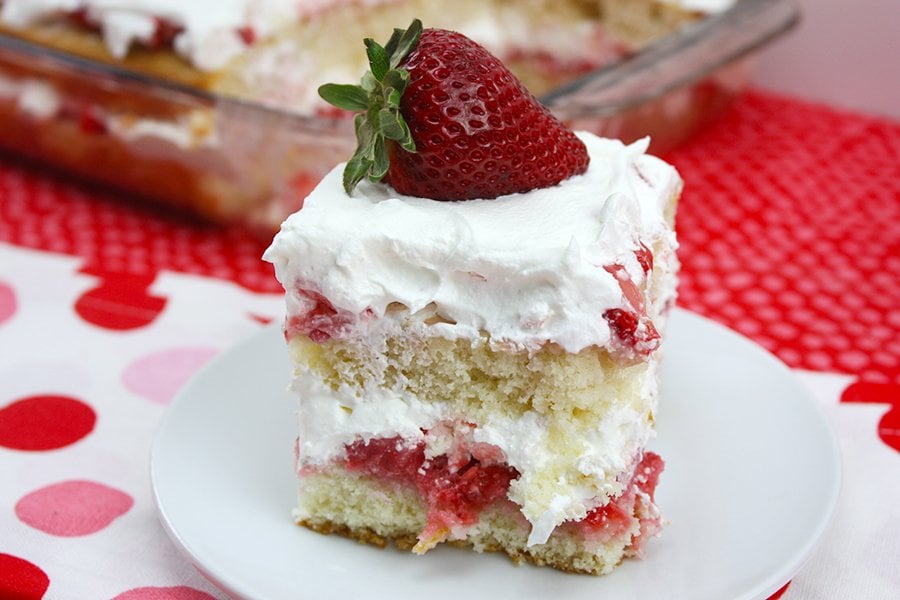 Homemade strawberry shortcake with a fresh strawberry on a white plate.