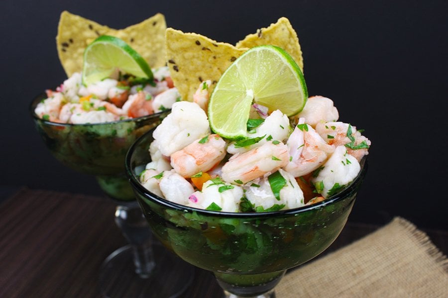 Ceviche in two green margarita glasses garnished with a lime slice and tortilla chips.