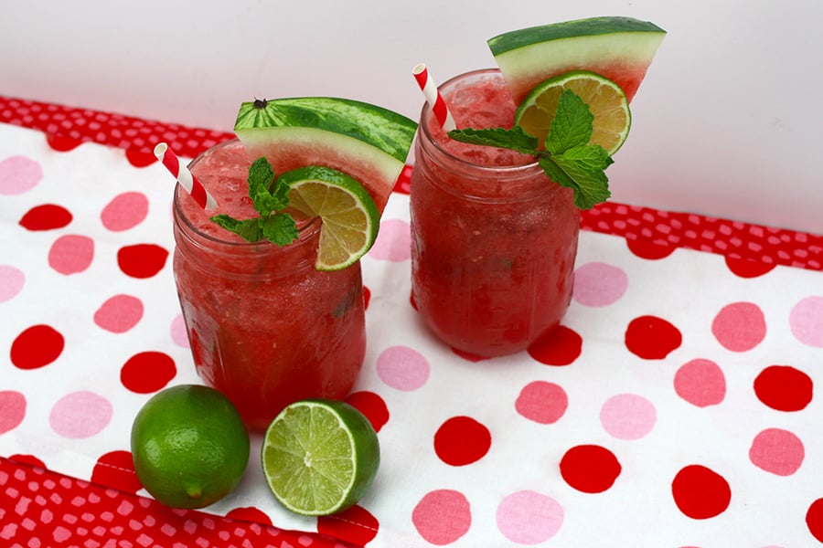 Watermelon Mojitos in glass mason jars garnished with mint, watermelon, and lime.