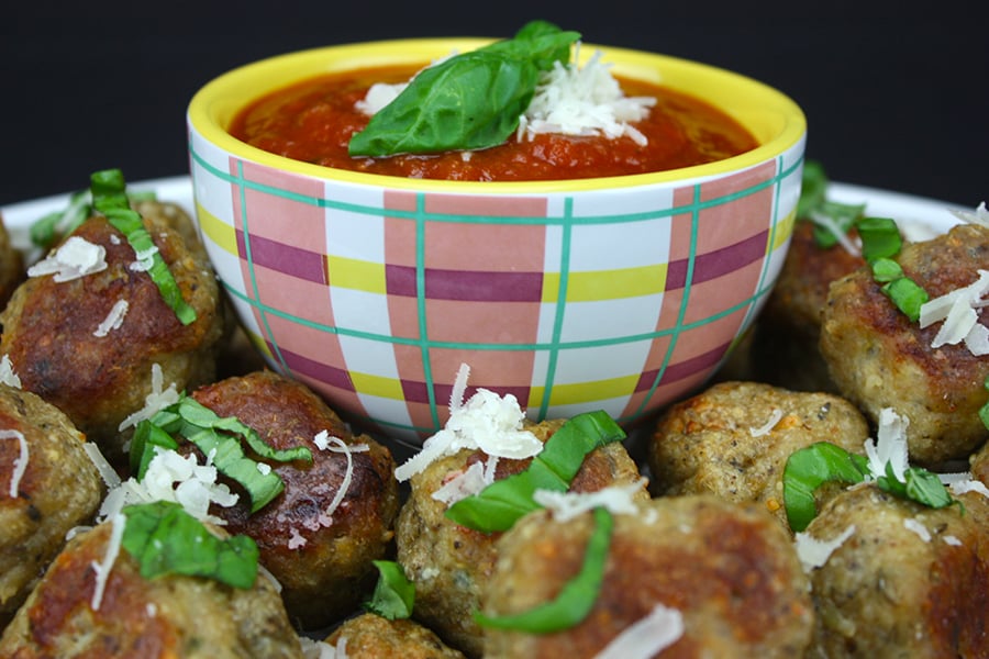 Chicken parmesan meatballs garnished with shredded cheese and basil.