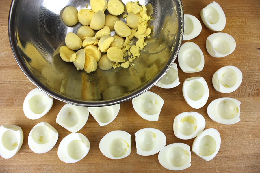 Deviled Eggs - egg yolks separated in a mixing bowl with the whites on a wooden cutting board