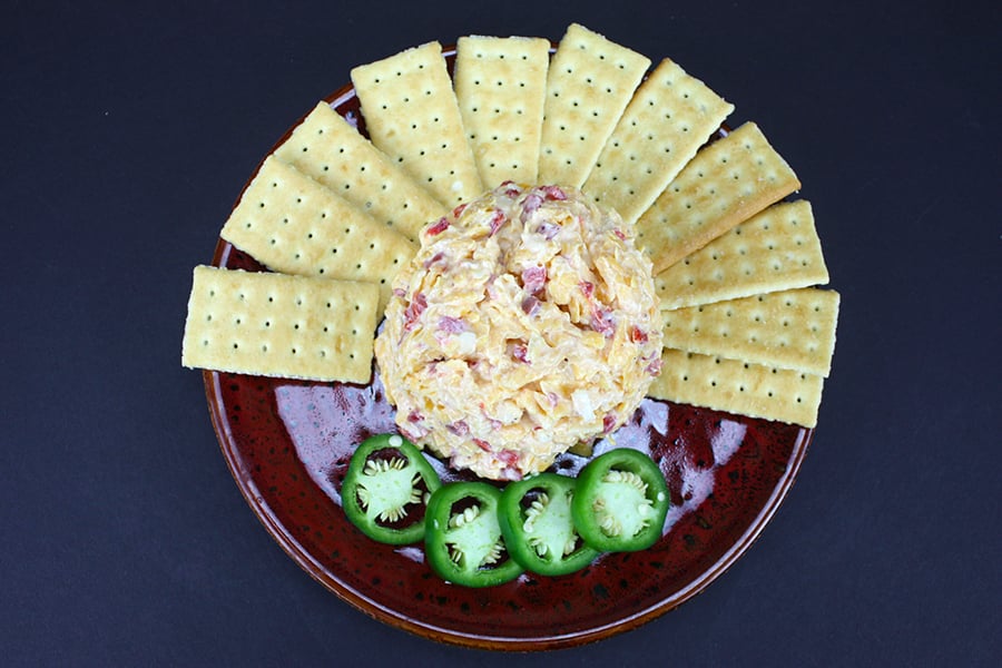 Pimento Cheese in the center of a red plate surrounded by crackers and sliced jalapeños.
