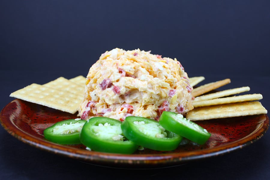 Pimento Cheese in the center of a red plate surrounded by crackers and sliced jalapeños.