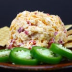 Homemade Pimento Cheese on a red plate with crackers and jalapeno slices.