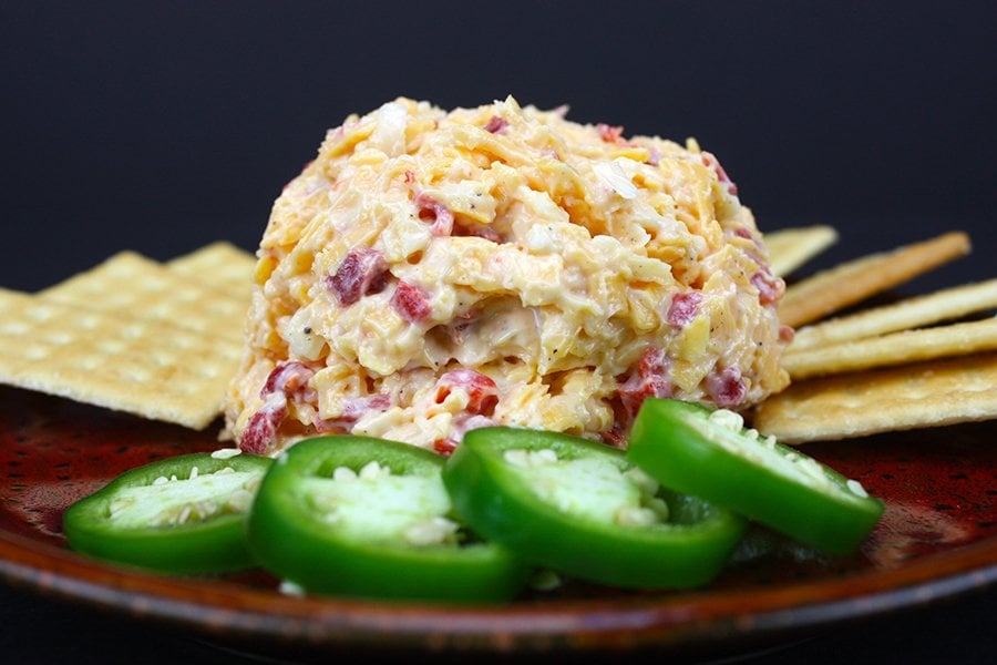 Homemade Pimento Cheese on a red plate with crackers and jalapeno slices.