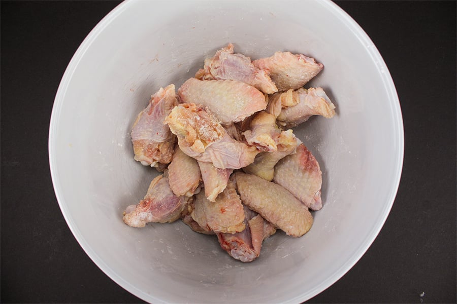 Raw wings coated in baking powder and salt in a white bowl.