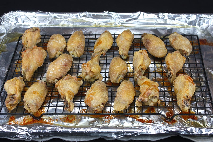Baked chicken wings tossed with buffalo sauce on a wire rack on a foil lined baking sheet.