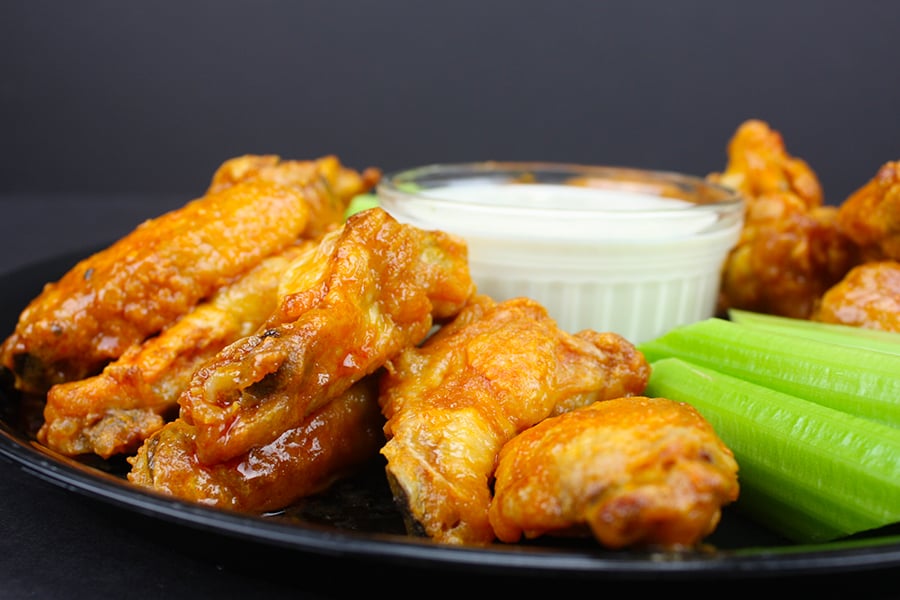 Crispy Oven Baked Chicken Wings on a round black platter with celery sticks and blue cheese dip.