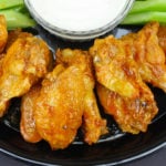 A plate of oven baked chicken wings with dipping sauce and celery on a dark plate.