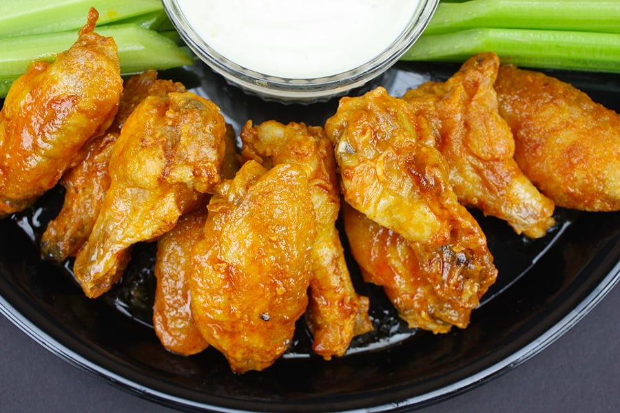 A plate of oven baked chicken wings with dipping sauce and celery on a dark plate.