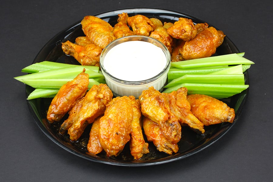 Crispy Oven Baked Chicken Wings on a round dark platter with celery sticks and blue cheese dip.