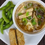 Hot and Sour Soup with spring rolls and edamame on a white plate.