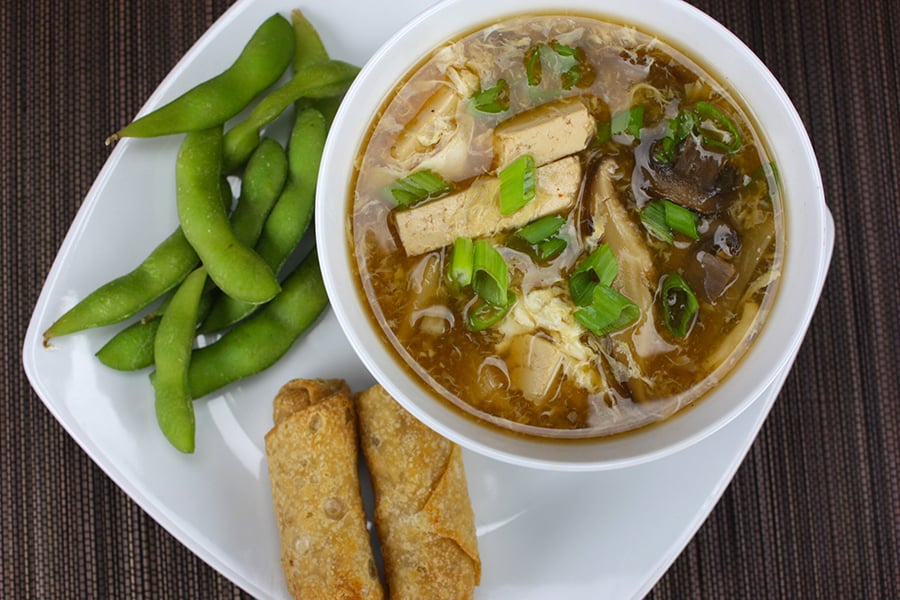 Hot and Sour Soup with spring rolls and edamame on a white plate.