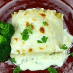 Lasagna Alfredo with broccoli served on a maroon plate.