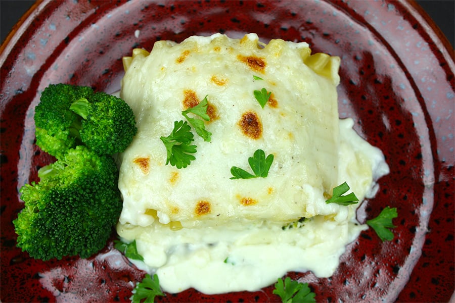 Lasagna Alfredo with broccoli served on a maroon plate.