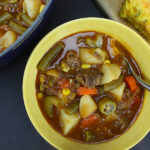 Vegetable beef soup with cornbread served in a yellow bowl.